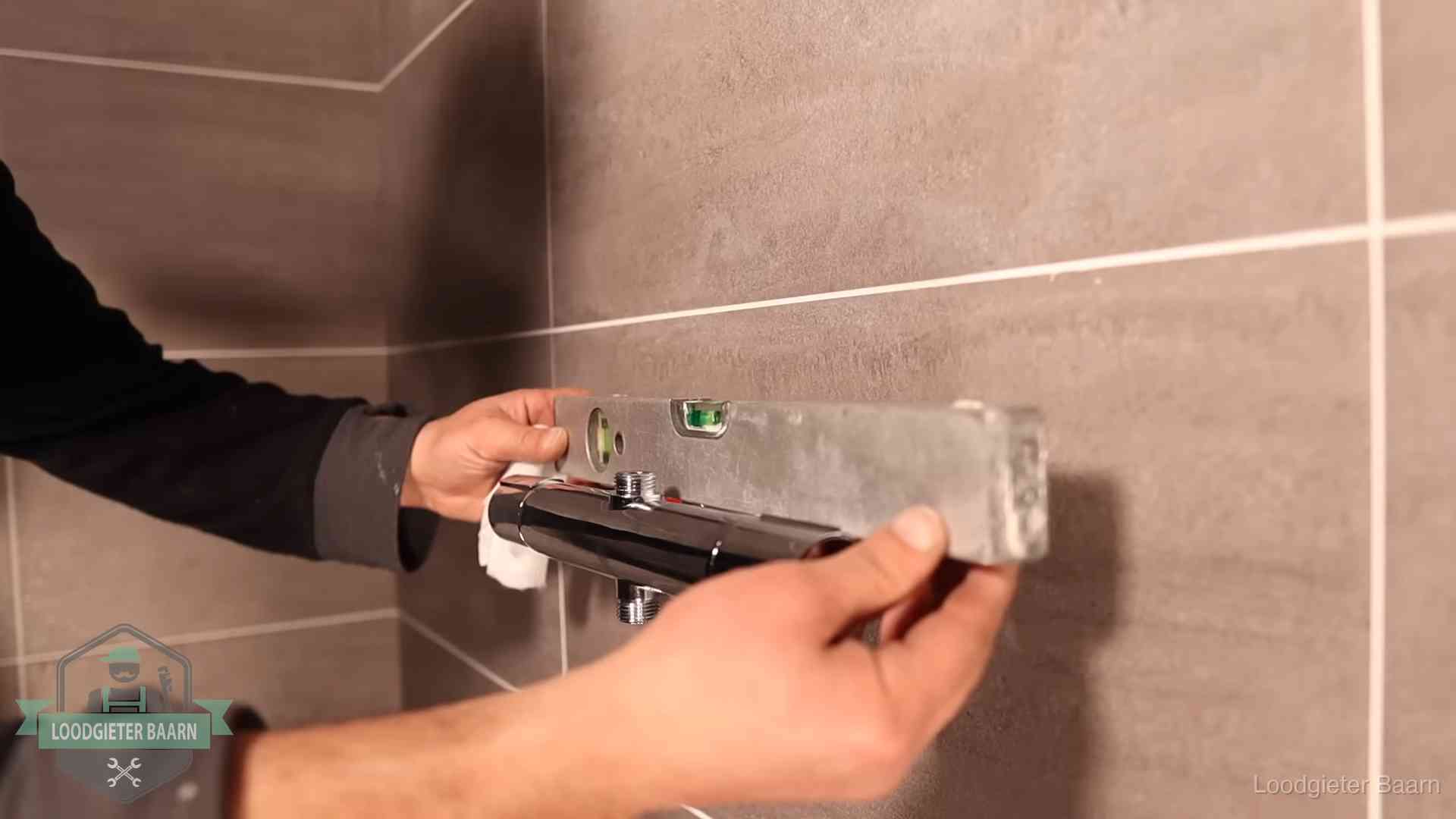 Loodgieter lijnt een douchekraan uit met een waterpas in een woning in Baarn