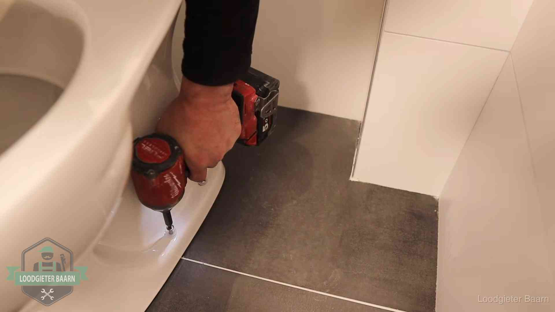 Kosten wc ontstoppen in Baarn Loodgieter zet de voet van een wc-pot vast op de tegelvloer in Baarn